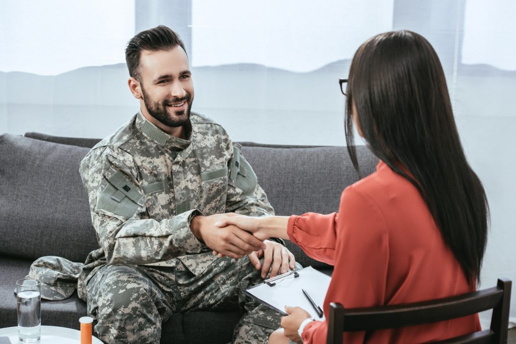 smiling soldier shaking hand of psychiatrist during therapy session